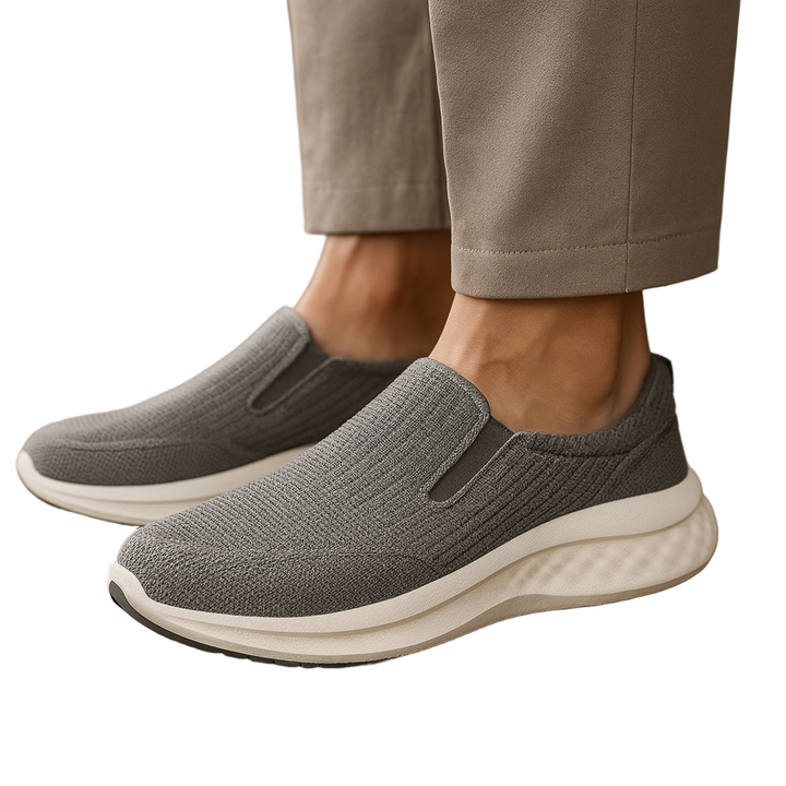 Gray slip-on sneakers with white soles worn with beige pants on a neutral background